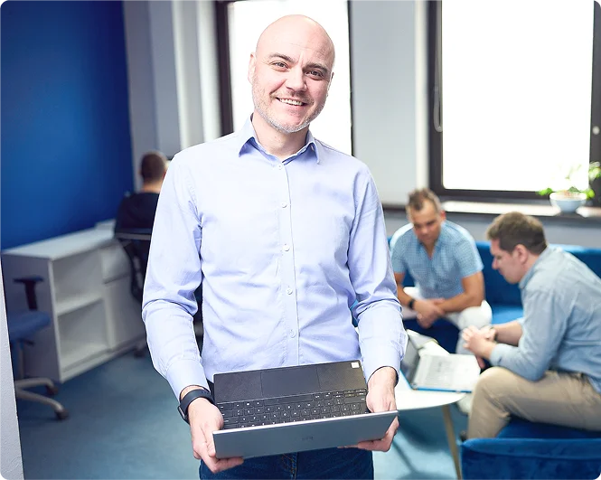 	Mężczyzna analizuje projekt na laptopie, a kobieta z kawą patrzy na ekran. Na biurku leżą próbki kolorów i materiały graficzne